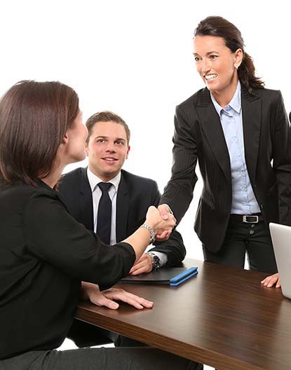 Two women executives shake hands across a table.
